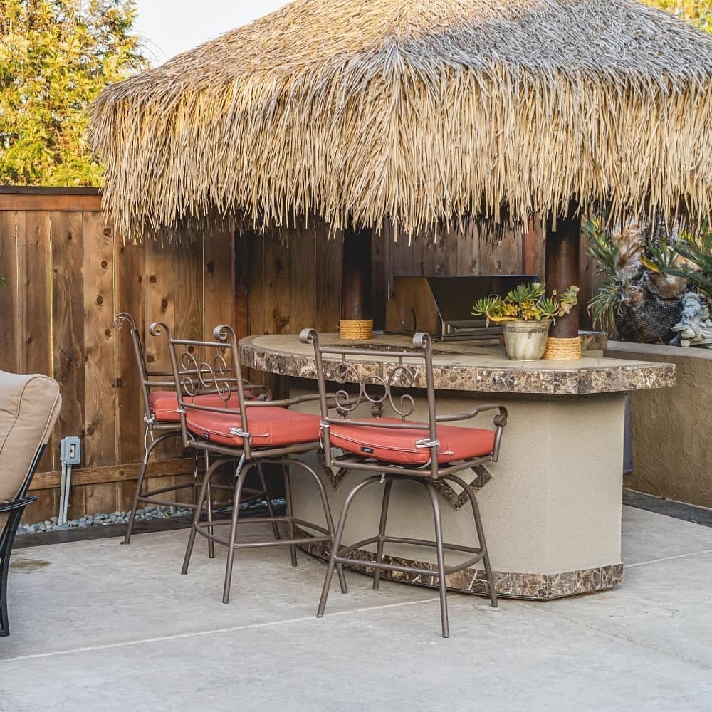 Tropical outdoor patio bar with thatched roof and metal bar stools, perfect for entertaining.