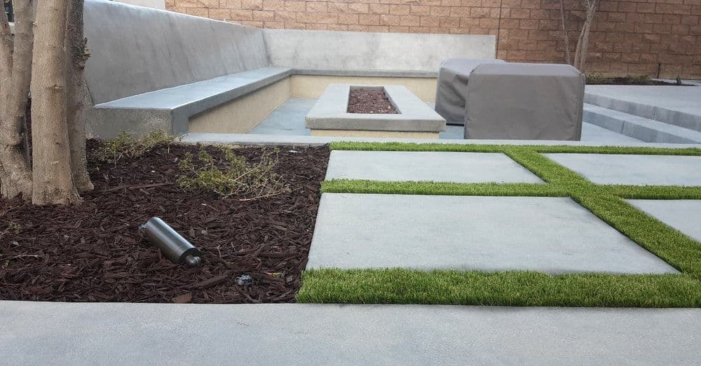 Modern outdoor patio featuring concrete seating, grass patches, and landscaped areas.