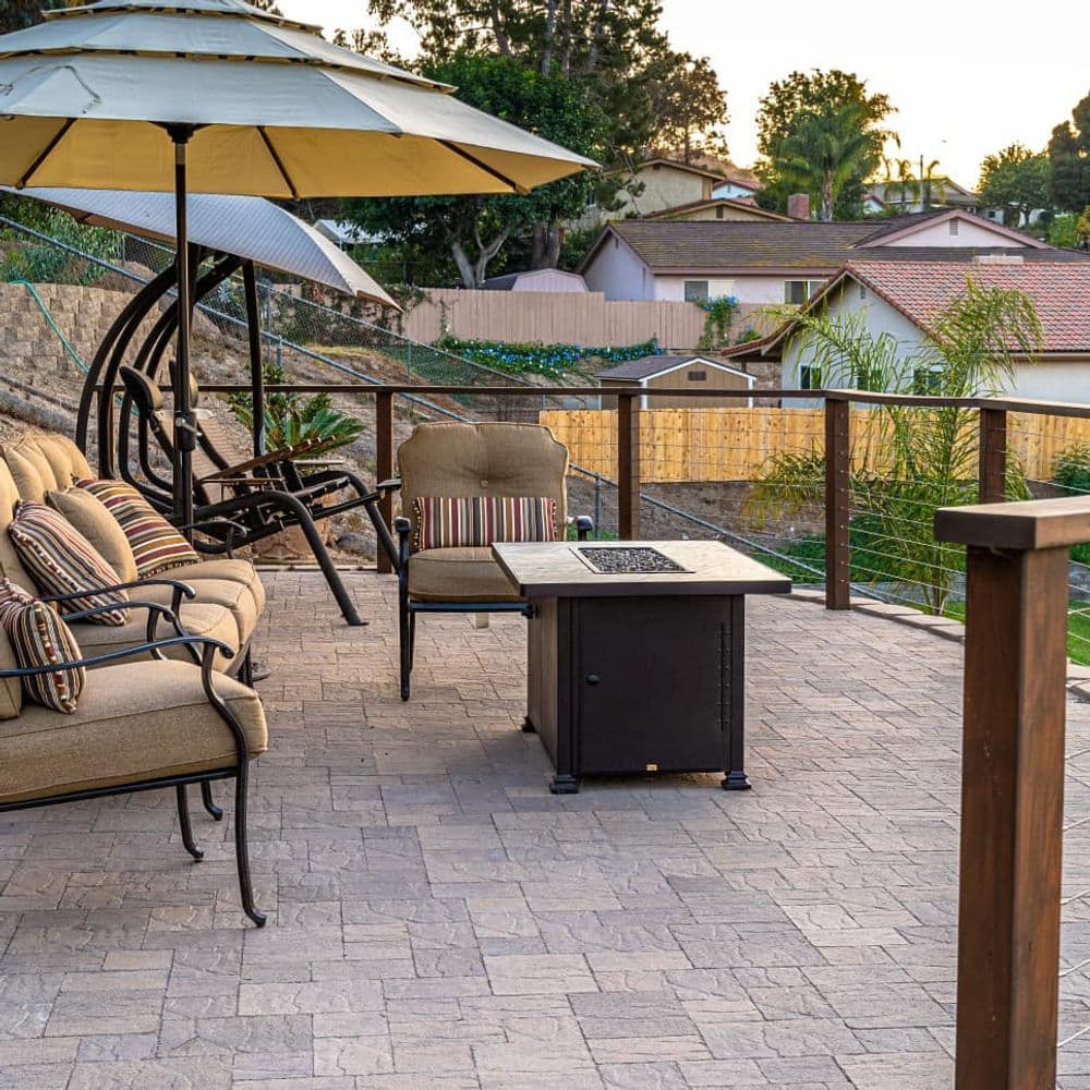 Cozy outdoor patio with seating, umbrella, and fire pit overlooking residential area.
