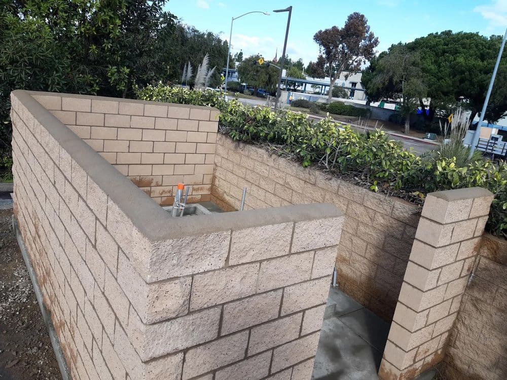 Newly constructed concrete block wall with fresh cement finish and landscaped surroundings.