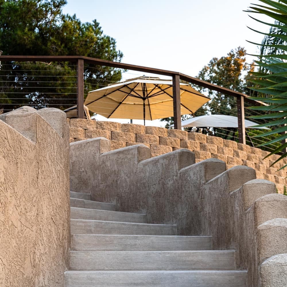 Elegant stone staircase leading to a patio with umbrellas and lush greenery.