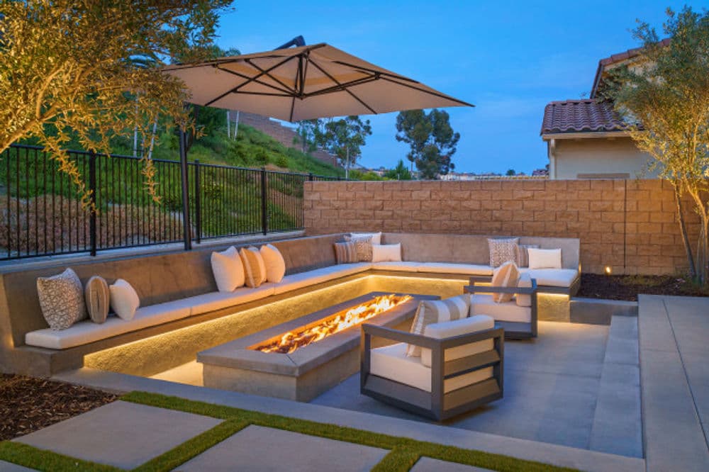 Modern outdoor seating area with fire pit, stylish cushions, and umbrella in landscaped yard.