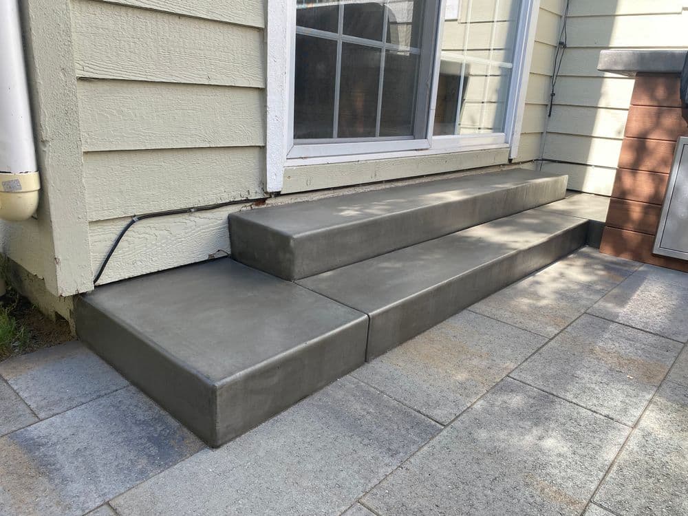 Concrete outdoor steps with three levels adjacent to a house and patio area.