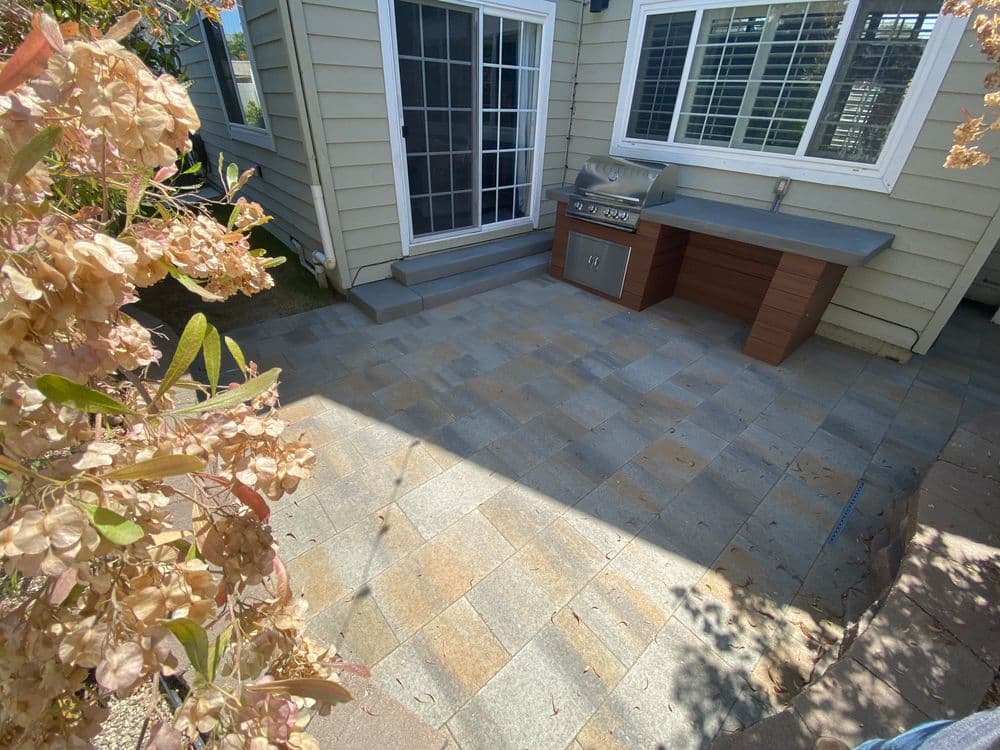 Patio area with grill and bar, surrounded by blooming flowers and house exterior.