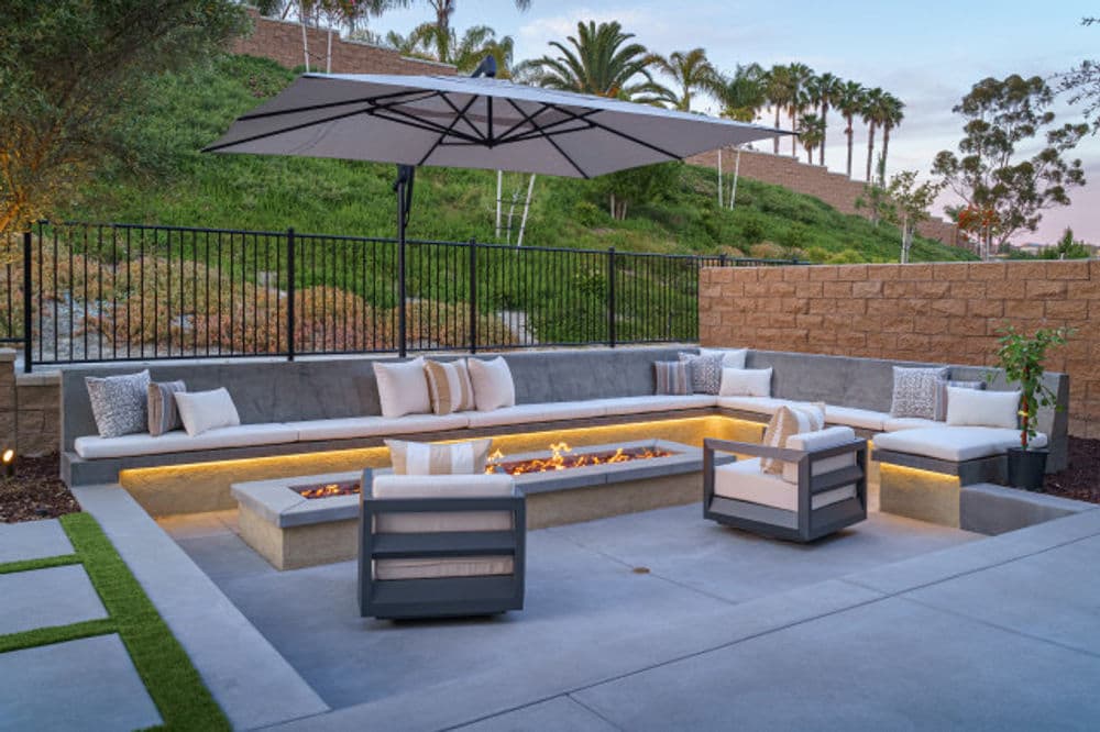 Modern outdoor living space with fire pit, seating, and umbrella in a landscaped garden.