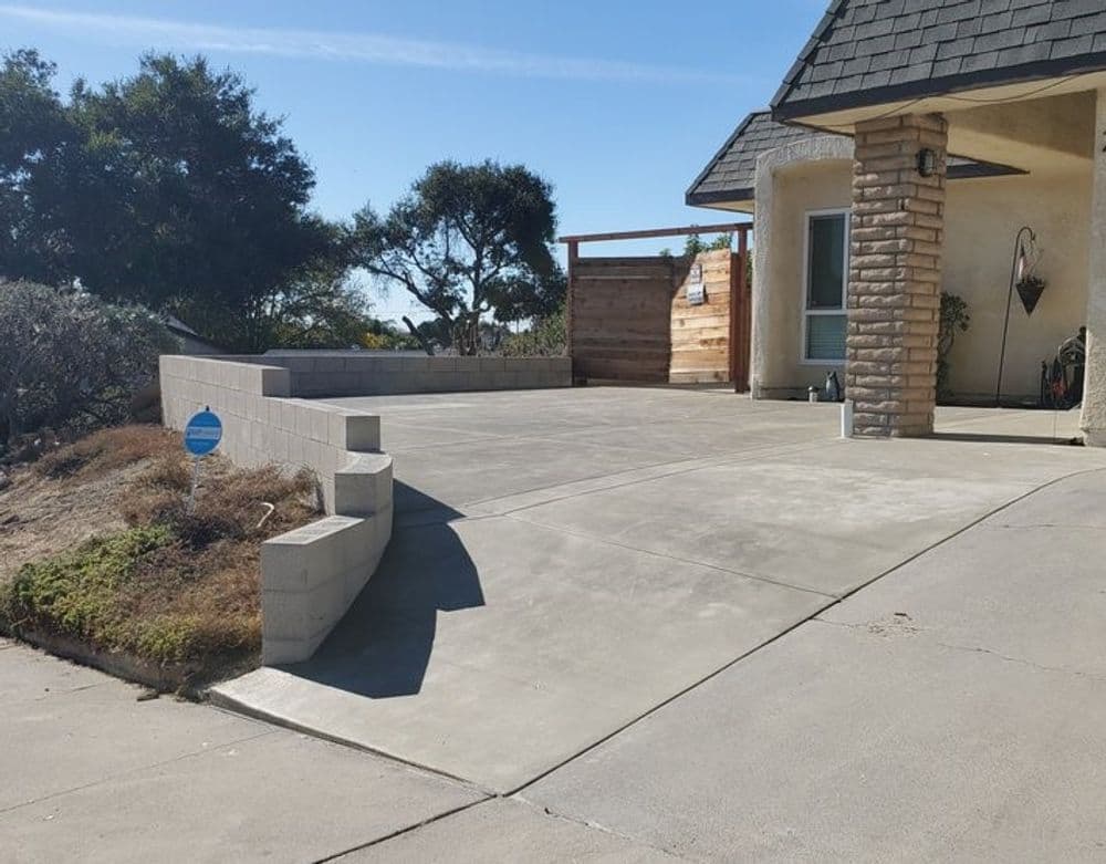 Concrete driveway leading to a house with landscaped surroundings and wooden fence.