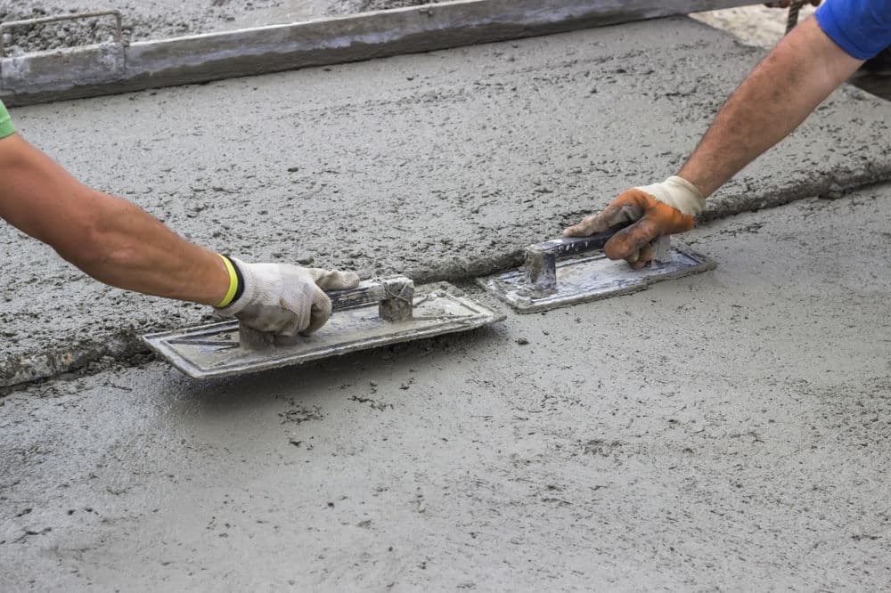 Workers smoothing freshly poured concrete with trowels on a construction site.