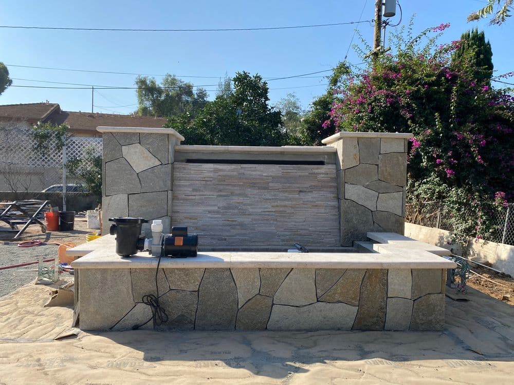 Outdoor stone fireplace with a sleek design, surrounded by landscaping and construction materials.