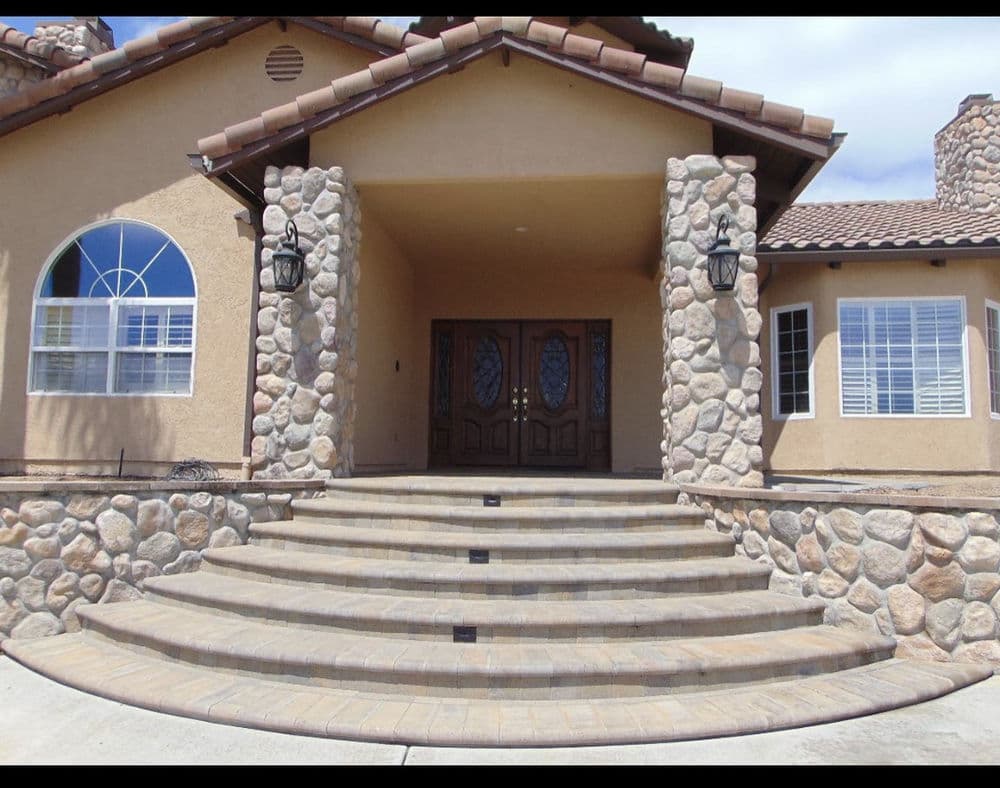 Elegant house entrance with stone accents, double doors, and landscaped stairs.