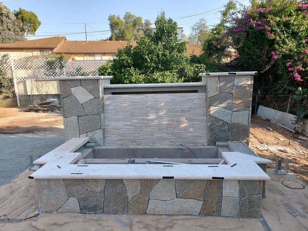 Outdoor stone fireplace with stone walls, modern design, and surrounding landscaping.