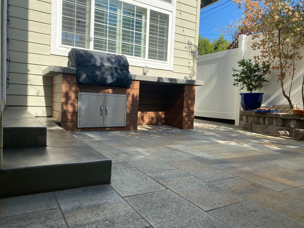 Patio renovation featuring a modern outdoor kitchen, stone flooring, and landscaped area.