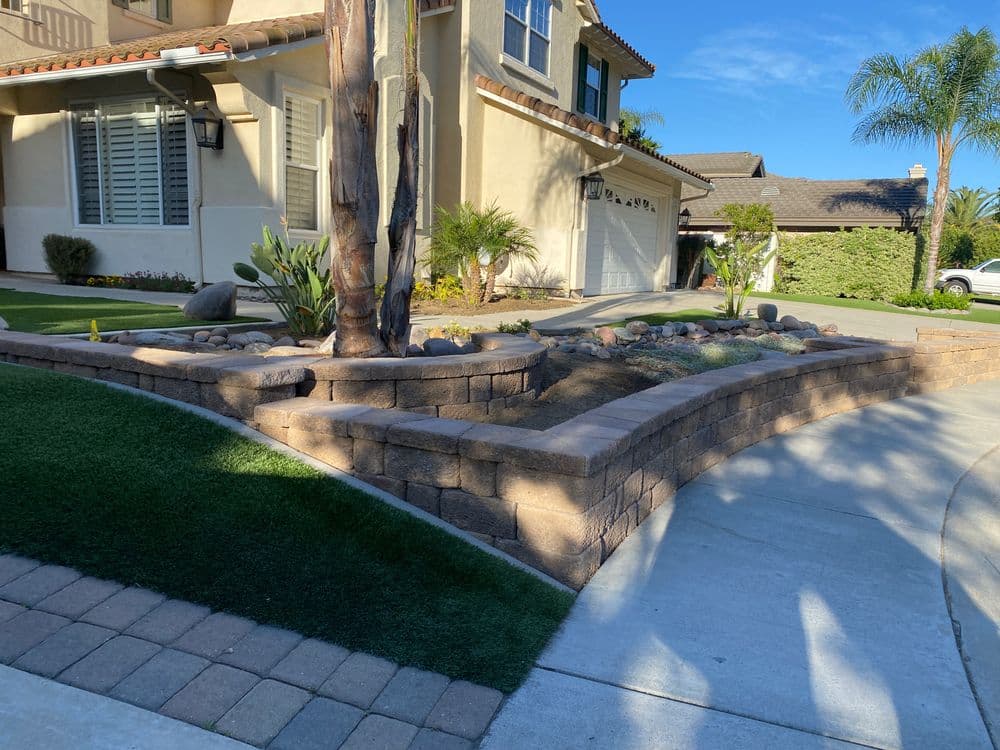 Landscaped front yard with stone retaining wall, palm tree, and manicured grass.
