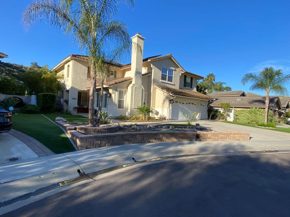 Two-story suburban home with palm trees, landscaping, and a circular driveway on a sunny day.