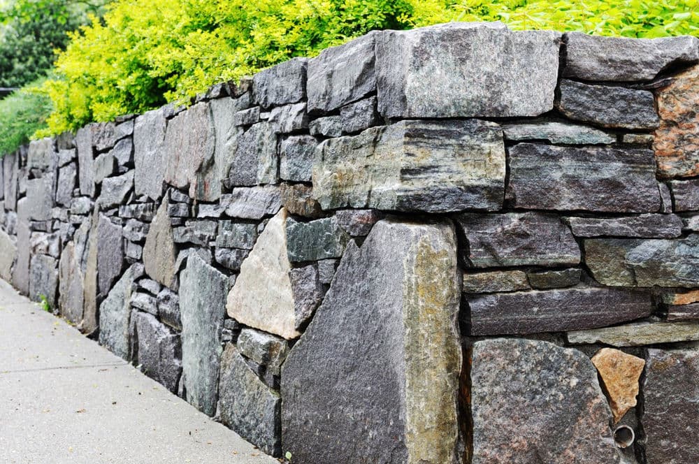 Natural stone wall with various textures, complemented by lush green shrubs above.
