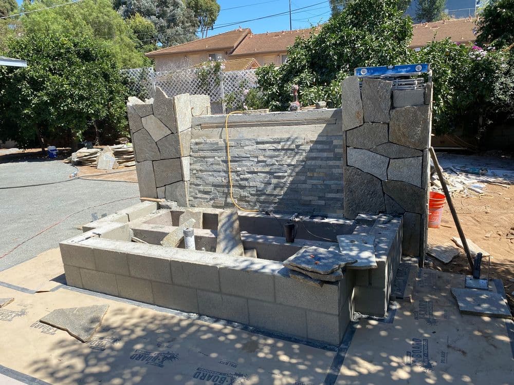 Stone masonry construction of an outdoor fireplace with stacked stone and cinder blocks.