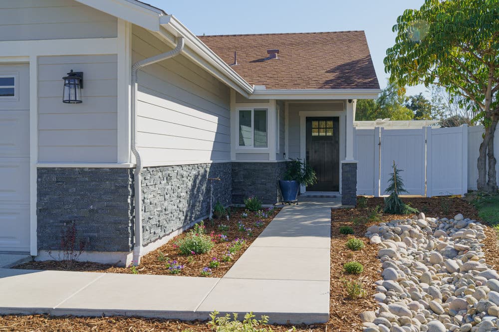 Modern home entrance with stone accents, lush landscaping, and a clear pathway.