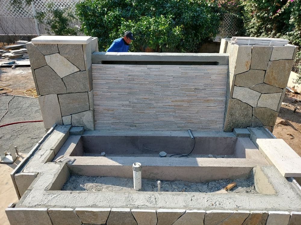Outdoor stone water feature installation in a residential garden, featuring a raised wall.