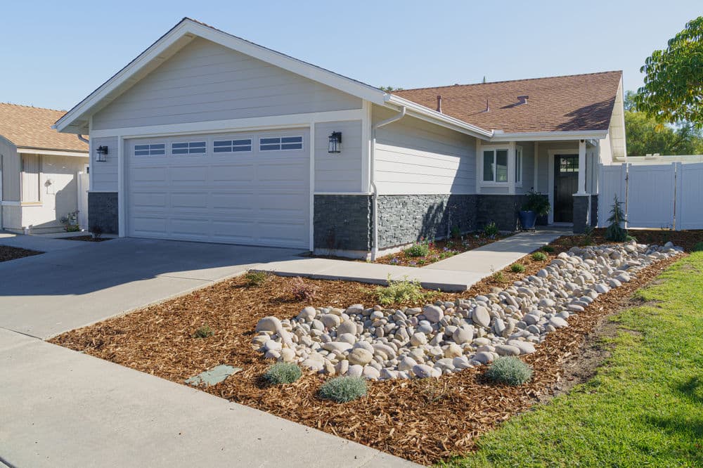 Modern single-story home with stone accents, landscaped rock garden, and a spacious driveway.