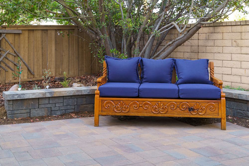 Wooden outdoor bench with blue cushions in a landscaped backyard setting.