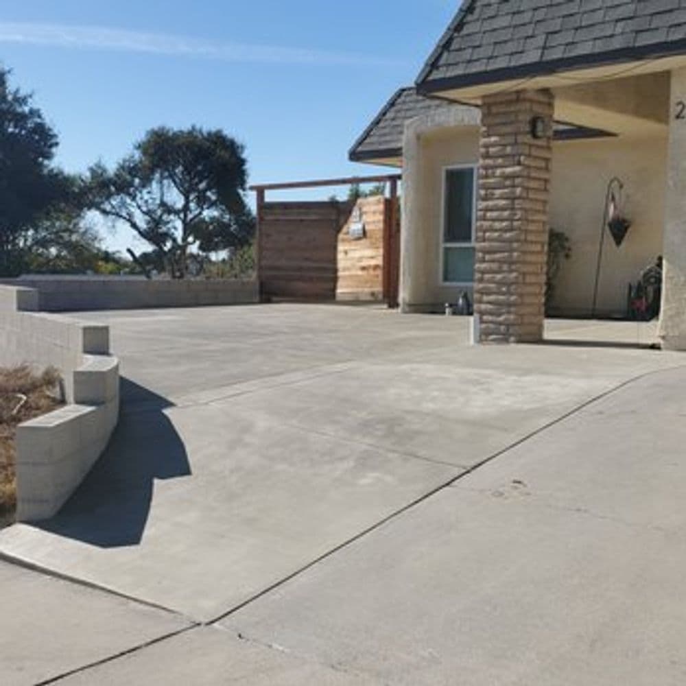 Concrete patio installation with landscaping and a wooden fence in a sunny outdoor setting.