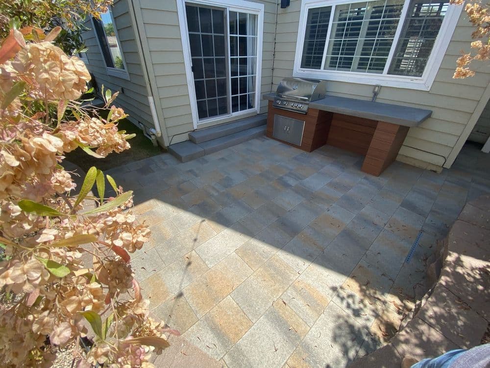 Patio area featuring stone tiles, outdoor grill, and nearby flowering plants.