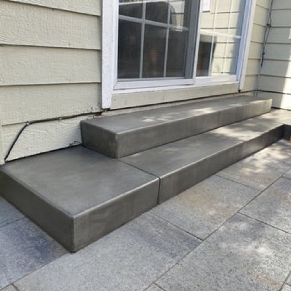 Concrete steps leading up to a house with a large window, showcasing modern design elements.