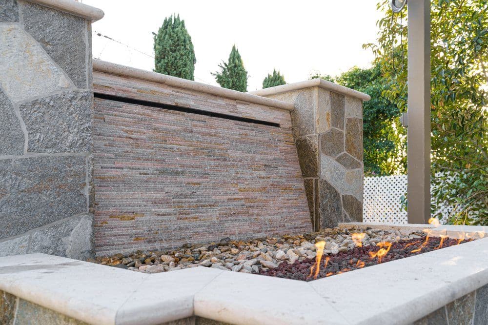 Modern outdoor stone fireplace with flowing water and decorative pebbles. Ideal for relaxation.