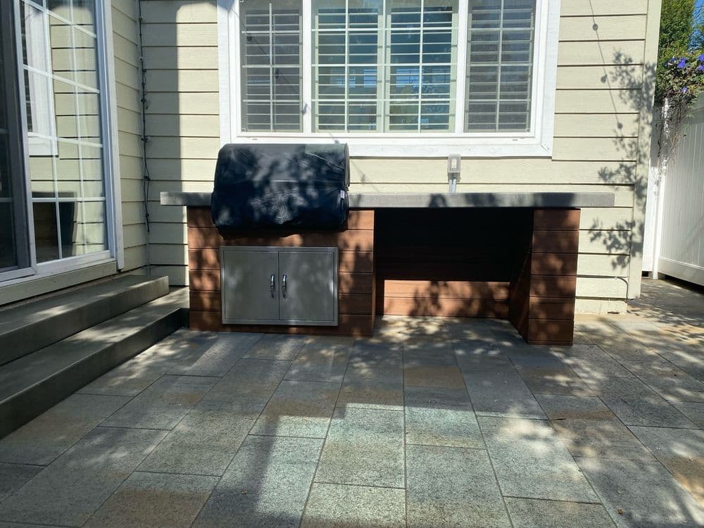 Outdoor kitchen setup with countertop, storage cabinet, and grill cover in a sunny patio area.
