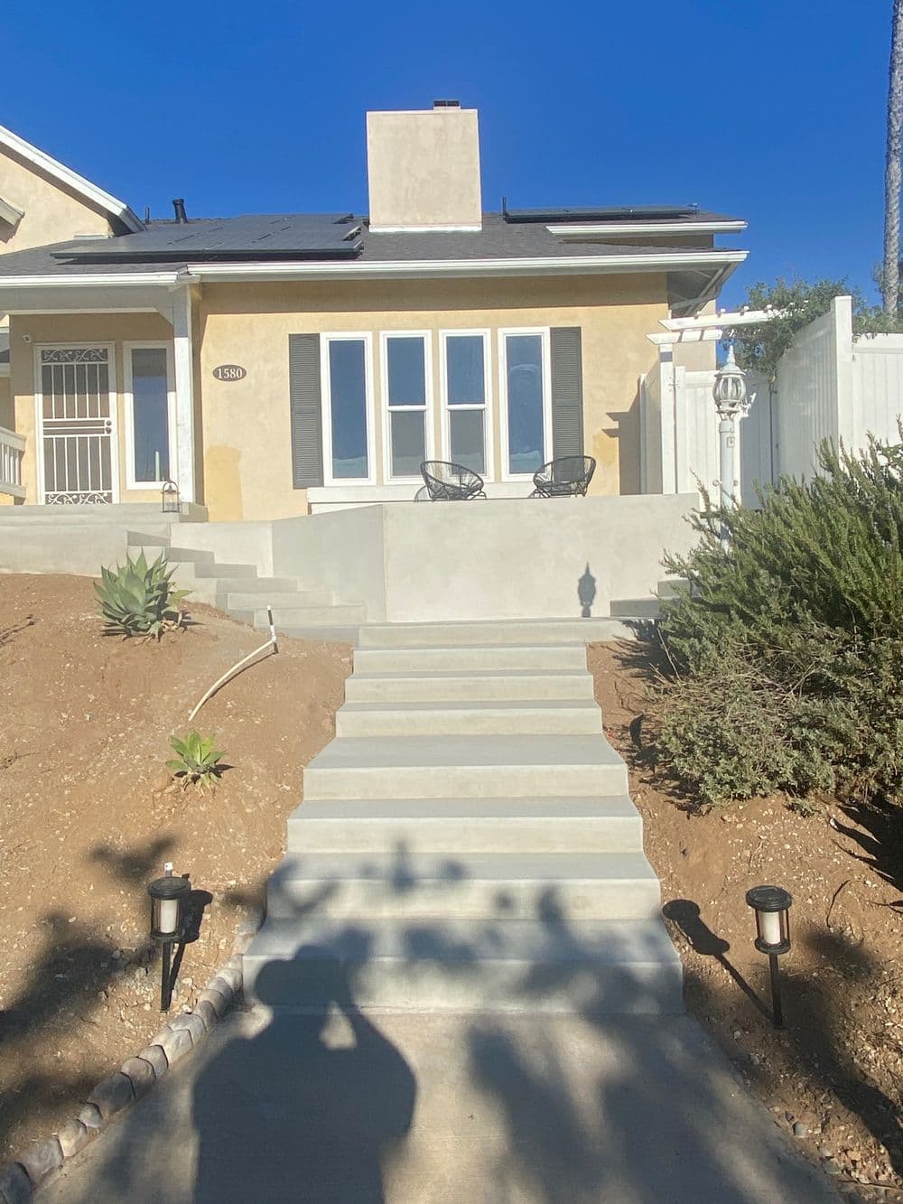 Modern front house exterior with steps, landscaping, and solar panels on the roof.