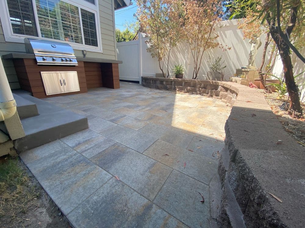 Patio area with grill, stone walls, and landscaped garden in a sunny outdoor setting.